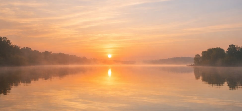 Peaceful sunrise over a calm lake with soft golden light and gentle mist, offering a serene and comforting scene often associated with funeral homes in Guilderland, NY